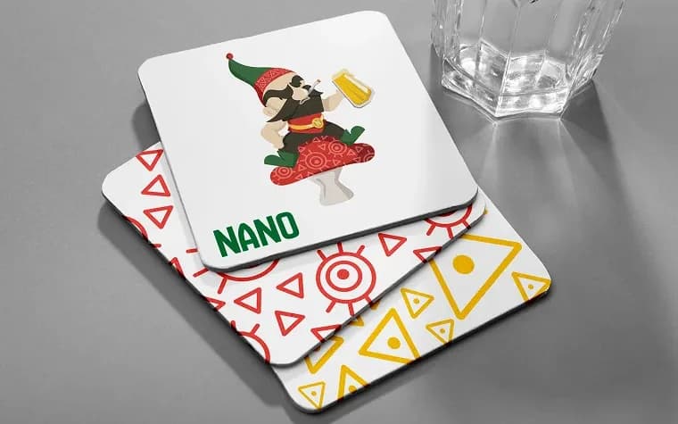 תחתיות כוס של NANO עם אלנאנו, הגמד עם הכובע האדום-ירוק, ודפוסים גיאומטריים בצבעי המותג (הדמיה)